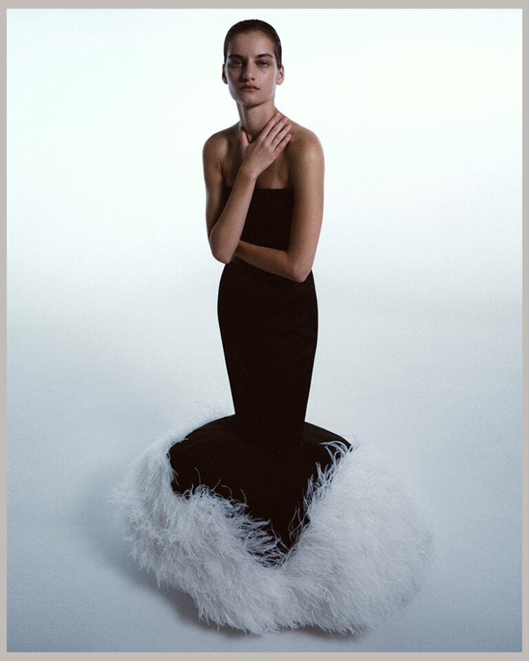 Photograph of a model in a skinny black dress with white feathers at the bottom