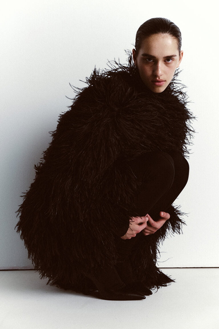 Photograph of a model in black feathers outfit in crouching pose