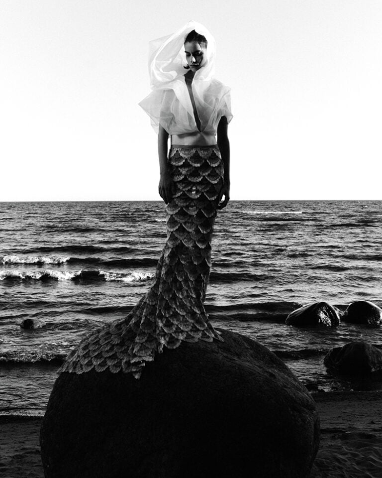 Black and white photograph of a model wearing mermaid dress on the seashore