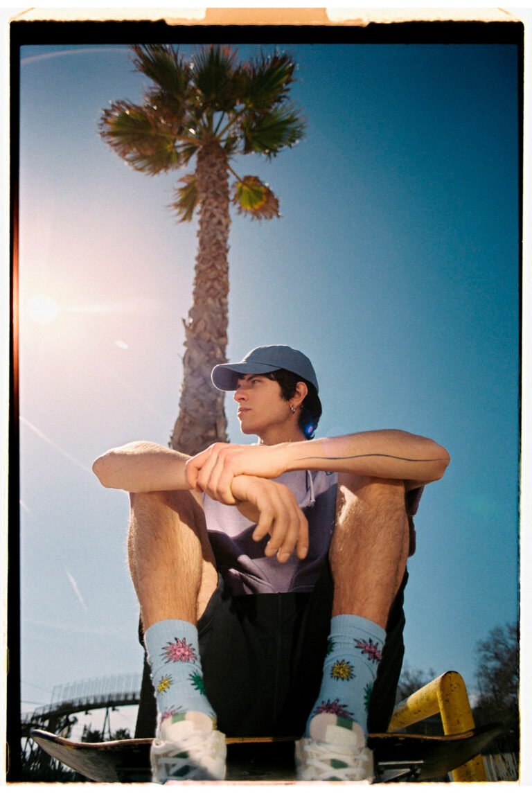 A young guy is sitting on the ground displaying his cool socks. Palm tree in the background. Urban fashion photoshoot.