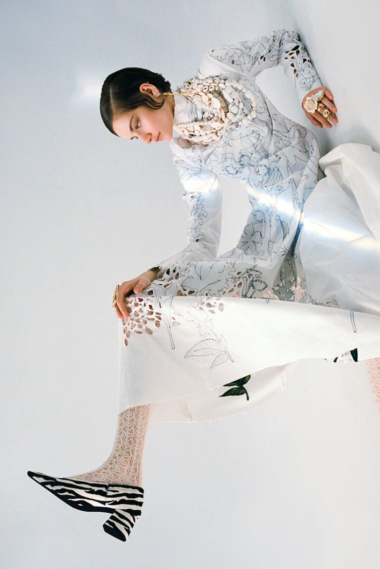 Photograph of a model in white with pieces of jewellery on her neck, ears and fingers