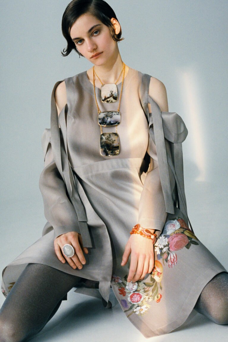 Photograph of a model in grey dress with large piece of jewellery on her neck