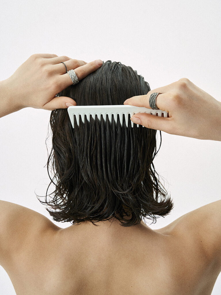 A young woman brushing her hair. There are a few rings on her fingers. Jewellery photography.