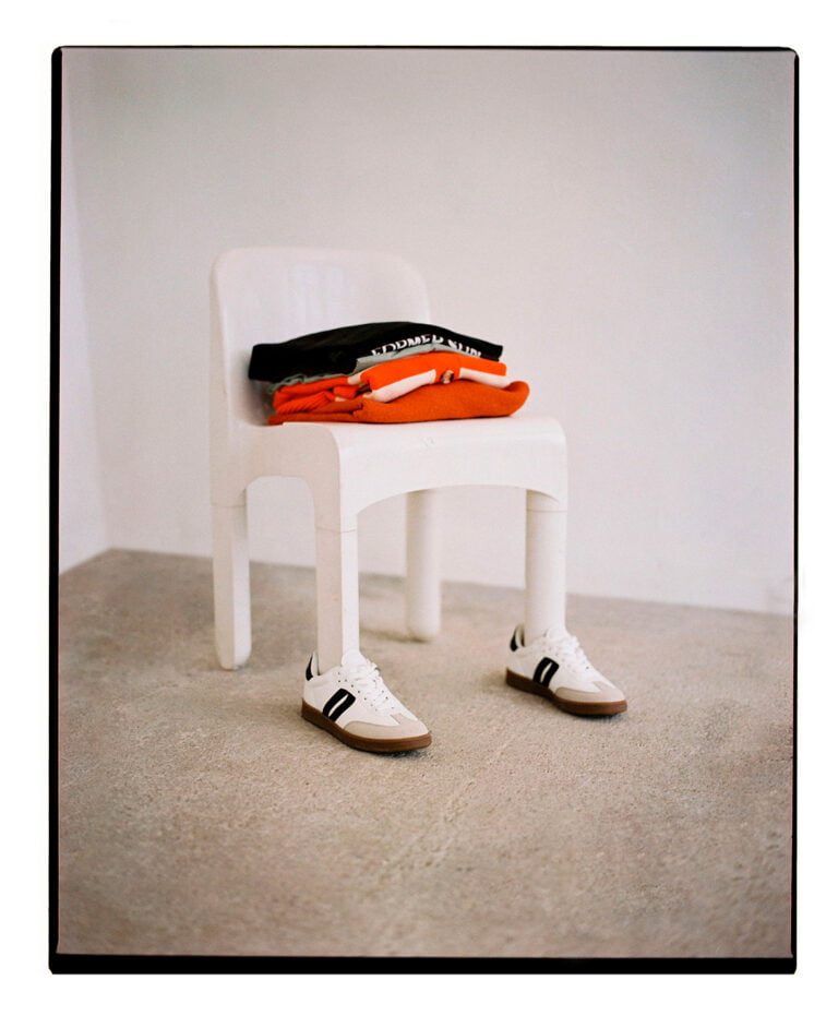 Small white chair wearing sneakers with a pile of clothes on top of it