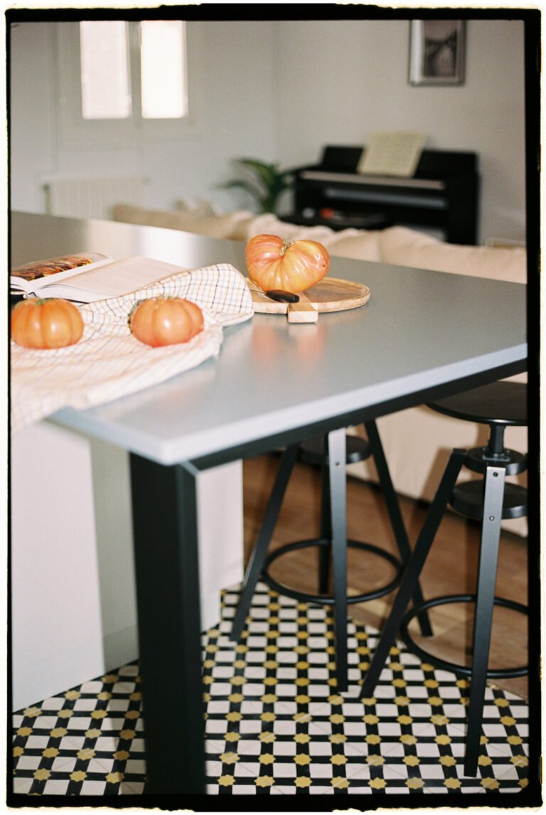 Modern kitchen table with three big tomatoes on it.