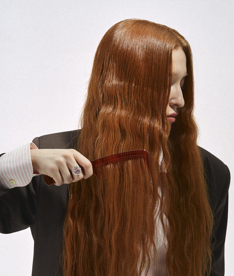 Model brushing her hair. There is a ring with a big pink stone on her finger. Jewellery photography.