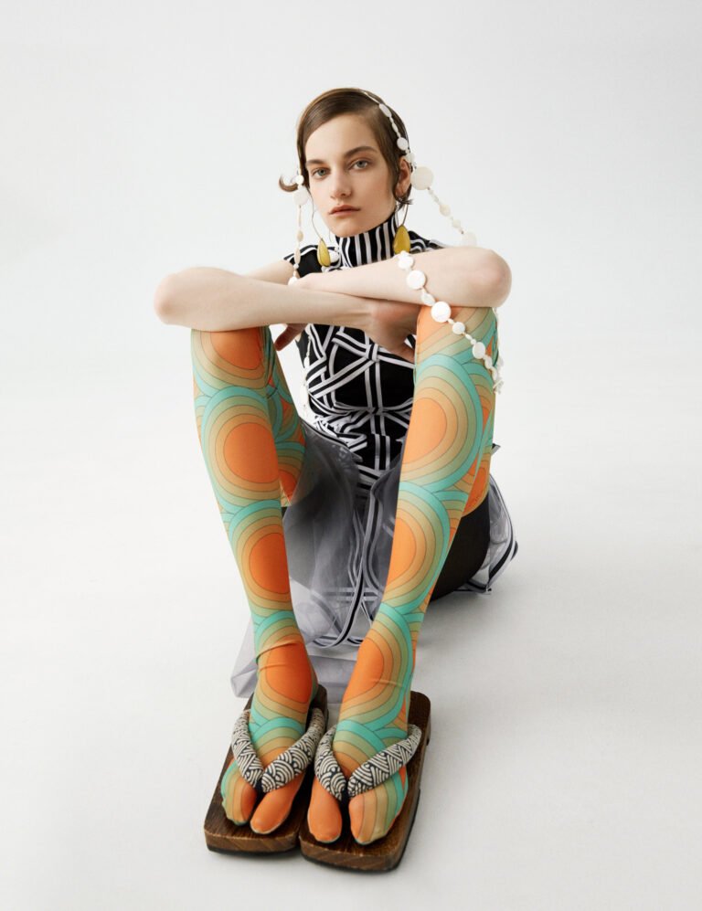 Photograph of a model in colourful tights sitting on the floor showing some jewellery